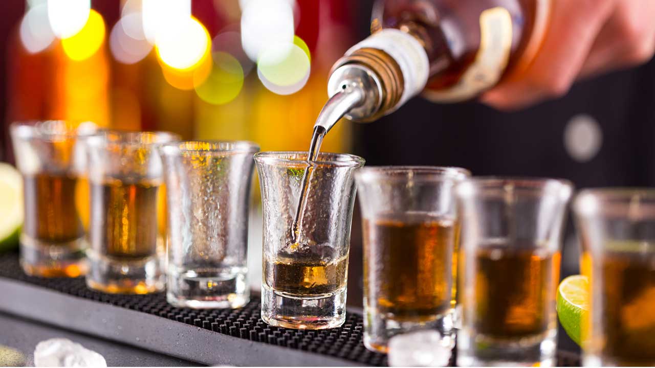 Bartender pouring whiskey shots onto 7 shot glasses