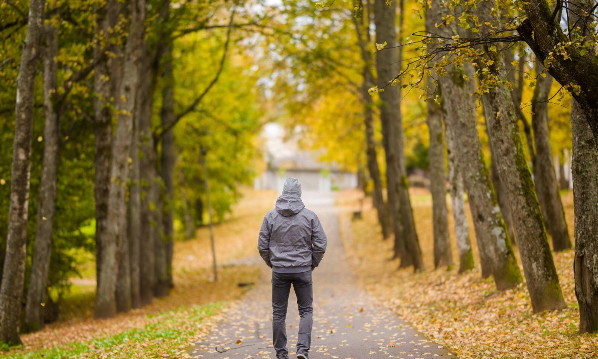 Man a wearing jacket walking through a park